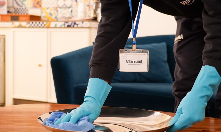 personale di impresa di pulizia intento a spolverare un tavolo di legno indossando guanti
