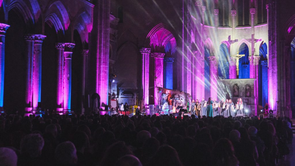 panoramica di una chiesa gotica illuminata dalle luci di un palco mentre si esibisce un coro gospel